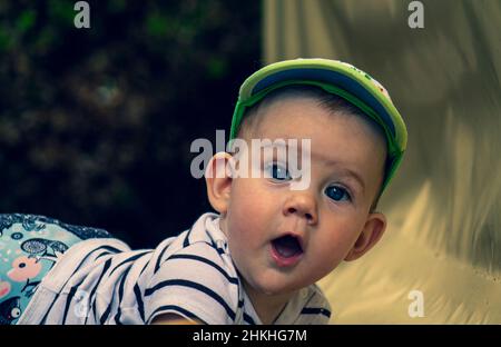 Überrascht niedliches Baby in einem Hut, der auf einem Bauch liegt und den Betrachter ansieht Stockfoto