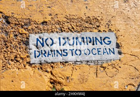 Kein Dumping – Schild „Drains to Ocean“ auf dem groben, gelb gestrichenen Gehweg Stockfoto