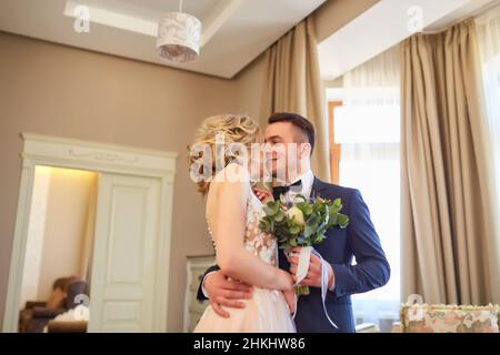 Wunderschöne Hochzeit, Mann und Frau, Braut und Bräutigam, die im Loft in der Nähe des Fensters stehen. Brautpaar verliebt. Der Bräutigam umarmt die Braut am Schoul Stockfoto