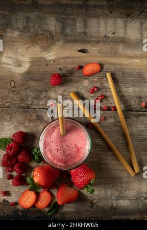 Smoothie-Getränk mit roten Beeren mit Bambusstrohhalmen, umgeben von grünen Zutaten, auf einer rustikalen Holzoberfläche, die flach von oben auf den Kopierraum gelegt ist Stockfoto
