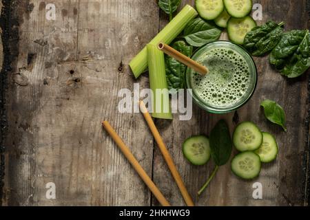 Grünes Smoothie-Getränk mit Bambusstrohhalmen, umgeben von grünen Zutaten, auf einer rustikalen Holzoberfläche, die flach von oben auf dem Kopierraum liegt Stockfoto