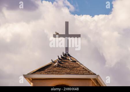 Tauben brüsten auf einem Dach und auf einem Kreuz gegen einen dramatischen bewölkten Himmel Stockfoto