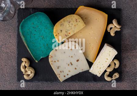 Auswahl an erlesenen Käsesorten auf einem Schieferteller auf braunem Hintergrund. Snacks für eine Weinparty Stockfoto