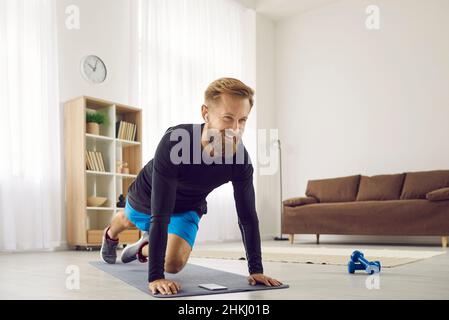 Porträt eines glücklichen, sportlichen Mannes, der kabellose Kopfhörer verwendet, während er zu Hause Sport macht. Stockfoto