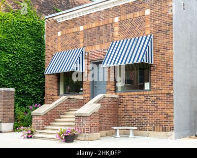 LANESBORO, MN - 26 AUG 2019: Frontfassade eines Bürogebäudes aus dem frühen 20th. Jahrhundert mit Backsteinarbeiten, Treppenhäusern, Blumen, Weinreben und Stockfoto