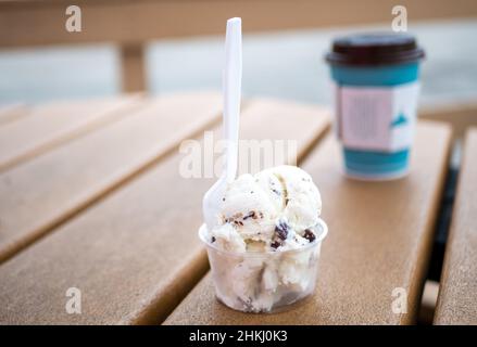 Plastiklöffel und -Tasse mit Vanille- und Schokoladenchip-Eis auf dem Picknicktisch Stockfoto
