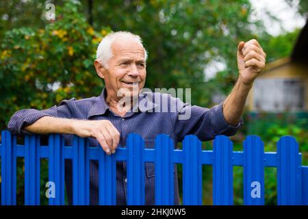 Alter Mann zeigt Faust im Freien neben dem Zaun Stockfoto