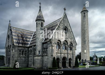 Schönes, altes Mausoleum mit keltischem Kreuz und rundem Turm auf dem Friedhof von Glasnevin, dramatischer Sturmhimmel im Hintergrund, Dublin, Irland Stockfoto