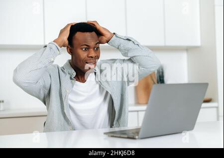 Angenehm überrascht junge Erwachsene Unternehmen afroamerikanischen Mann, Manager, Broker sitzt am Tisch in einer überraschten Pose, mit Laptop, schockiert durch gute Nachrichten oder Nachrichten, bekam finanzielle Gewinn, aufgeregt. Stockfoto