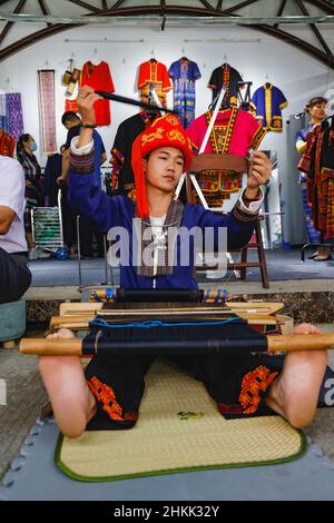 (220205) -- HAIKOU, 5. Februar 2022 (Xinhua) -- das Aktenfoto zeigt Huang Yangwei, einen 24-jährigen Mann der ethnischen Minderheit von Li, der am 27. November 2021 in der südchinesischen Provinz Hainan den ethnischen Brokat von Li webt. Das immaterielle kulturelle Erbe des Li Brokates kann bis vor über 3.000 Jahren zurückreichen. Im Einklang mit der Li-Tradition werden die Brokatwebtechniken nur „an Frauen weitergegeben, nicht an Männer“, wie im alten China Männer auf der Farm arbeiten sollten, während Frauen geweben sollten. In den letzten Jahren haben die Bildungsbehörden in Hainan den örtlichen Schulen den traditionellen Brokat eingeführt Stockfoto