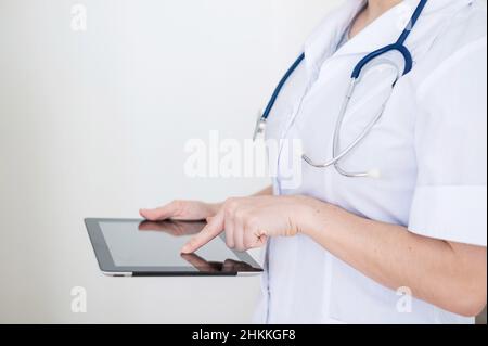 Nicht erkennbare Ärztin in Uniform verwendet einen Tablet-Computer. Ein medizinischer Mitarbeiter kontaktiert Patienten auf einem Gerät. Abgeschnitten. Stockfoto