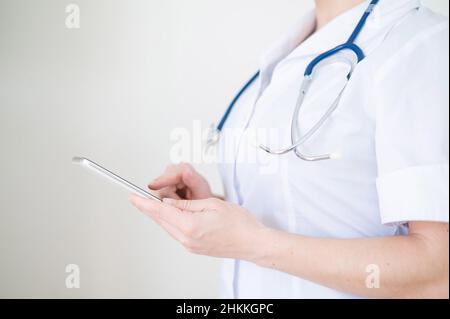 Nicht erkennbare Ärztin benutzt Handy. Der Arzt kommuniziert mit den Patienten über ein Smartphone. Abgeschnitten. Stockfoto