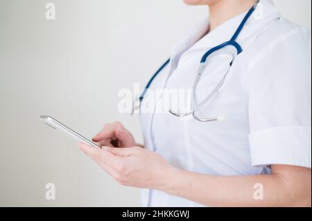 Nicht erkennbare Ärztin benutzt Handy. Der Arzt kommuniziert mit den Patienten über ein Smartphone. Abgeschnitten. Stockfoto