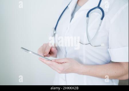 Nicht erkennbare Ärztin benutzt Handy. Der Arzt kommuniziert mit den Patienten über ein Smartphone. Abgeschnitten. Stockfoto