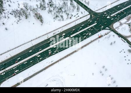 autobahnkreuzung im schneebedeckten Vorstadtbereich mit Autoverkehr. Luftaufnahme. Stockfoto