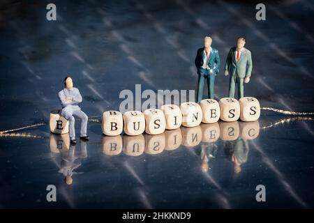 Miniatur-Modell von Geschäftsleuten und Holzwürfel mit e Business Inschrift auf einem Faden auf reflektierenden Tisch aufgereiht. Das Online-Geschäftskonzept. Stockfoto