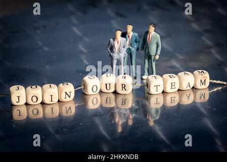 Miniatur-Modell von Geschäftsleuten und Holzwürfel mit Join unserem Team Inschrift auf einem Faden auf reflektierenden Tisch aufgereiht. Das Rekrutierungsgeschäft concep Stockfoto