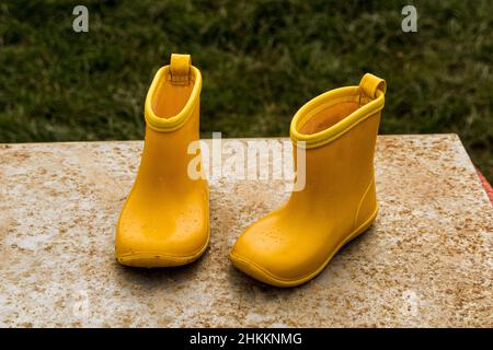 Nahaufnahme einer gelben Gummistiefel für Kinder auf einer Steinbank im Garten Stockfoto