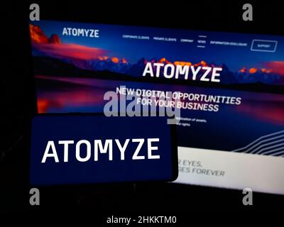 Person, die Smartphone mit Logo des Schweizer Technologieunternehmens ATOMYZE AG auf dem Bildschirm vor der Website hält. Konzentrieren Sie sich auf die Telefonanzeige. Stockfoto