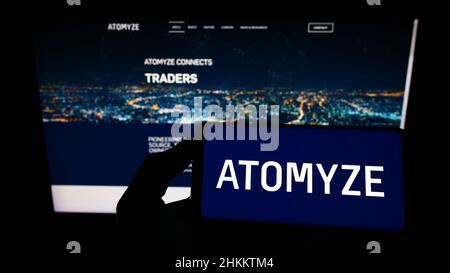 Person, die Mobiltelefon mit Logo des Schweizer Technologieunternehmens ATOMYZE AG auf dem Bildschirm vor der Business-Webseite hält. Konzentrieren Sie sich auf die Telefonanzeige. Stockfoto