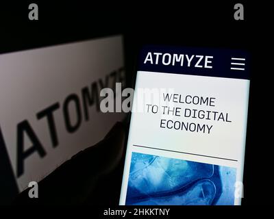 Person, die Smartphone mit der Webseite des Schweizer Technologieunternehmens ATOMYZE AG auf dem Bildschirm vor dem Logo hält. Konzentrieren Sie sich auf die Mitte des Telefondisplays. Stockfoto