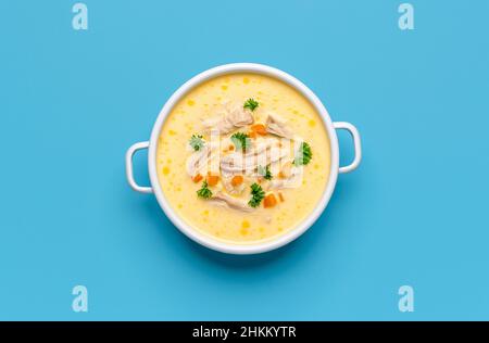 Blick von oben mit einer Schale griechischer Hühnersuppe, minimalistisch auf einem blauen Tisch. Köstliche Avgolemono-Suppe, zubereitet aus Hühnerfleisch, Zitrone, Eiern und Reis Stockfoto