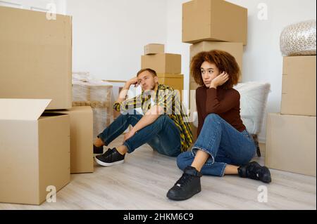 Müdes multirassisches Paar, das zwischen Kartons sitzt Stockfoto