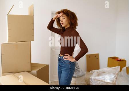 Müde junge Frau, die zwischen Kartons steht Stockfoto