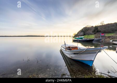 Ein spektakulärer Blick auf das ruhige Wasser eines Sees bei Sonnenaufgang mit mehreren Fischerbooten im Vordergrund. Stockfoto