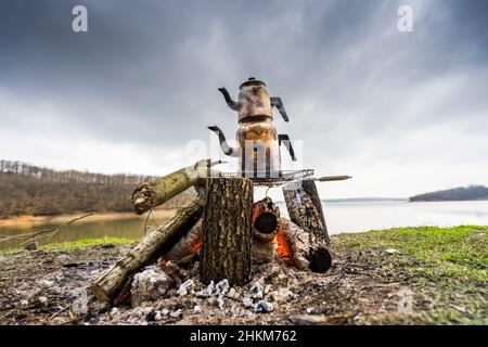 Türkische traditionelle Teekannen kochten am Lagerfeuer, ein glatter See im Hintergrund. Stockfoto