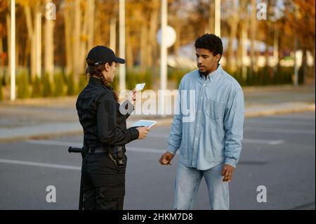 Weiblicher Polizist, der das Ausweisdokument der männlichen Passanten überprüft Stockfoto