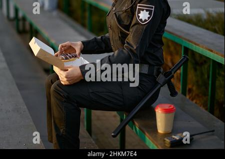 Polizeibeamter, der in der Nähe des Parks Donut isst Stockfoto