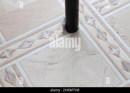 Gerissenes Linoleum. Stuhlbein und zerrissenes Linoleum. Loch im Linoleum. Stuhl auf dem Boden. Die Spuren der Verwendung der Bodenbeläge. Verschleißfestigkeit. Schutz agai Stockfoto