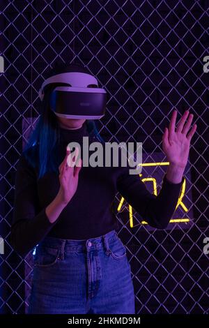 Teen Mädchen mit vr Headset ist in der virtuellen Realität Cyberspace futuristischen neon bunten Hintergrund. Das Konzept der Metaverse, Virtual Reality, Virtua Stockfoto