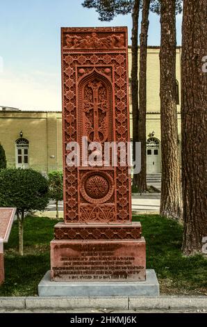 Isfahan, Nor Julfa, Iran, 16. November 2021: Khachkar aus rotem Tuff mit einem durchbrochenen Kreuz in einem Korbrahmen mit einem runden Symbol der Ewigkeit, Gesichter Stockfoto