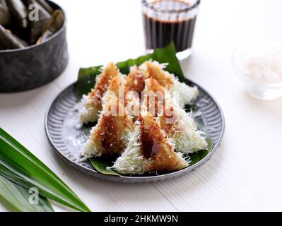 Lupis, indonesischer traditioneller Snack aus klebriges Reis, verpackt mit Bananenblatt, Shape Triangle serviert mit flüssigem Palmzucker und geriebener Kokosnuss Stockfoto