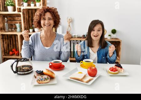 Familie von Mutter und Down-Syndrom Tochter zu Hause sitzen Frühstück feiern überrascht und erstaunt über den Erfolg mit den Armen angehoben und offen ey Stockfoto