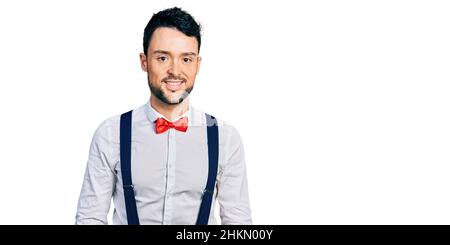 Hispanic Mann mit Bart trägt Hipster-Look mit Fliege und Hosenträger mit einem glücklichen und kühlen Lächeln im Gesicht. Glückliche Person. Stockfoto