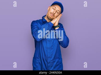 Glatze Mann mit Bart tragen Baumeister Jumpsuit Uniform schlafen müde träumen und posieren mit den Händen zusammen, während lächeln mit geschlossenen Augen. Stockfoto