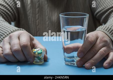 Ein Mann sitzt an einem Tisch und hält ein Glas Wasser und Pillen in den Händen. Stockfoto