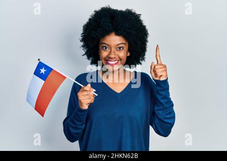 Junge afroamerikanische Frau, die die chilenische Flagge hält, lächelt mit einer Idee oder Frage, die mit dem Finger und einem glücklichen Gesicht zeigt, Nummer eins Stockfoto