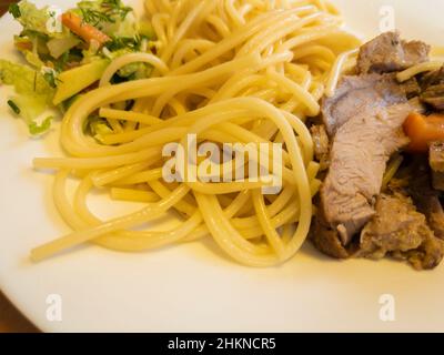 Blick aus der Nähe auf dem Teller mit Pasta, gebackenem Fleisch und Gemüsesalat Stockfoto