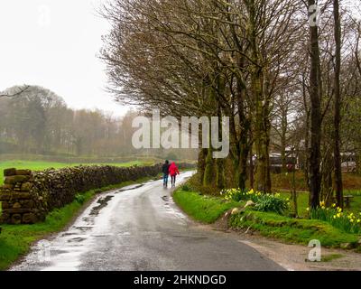 Zwei Personen, die nach einem Regensturm im Lake District, Großbritannien, auf einer nassen Straße spazieren Stockfoto