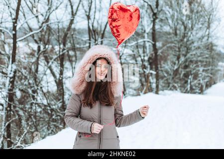 Mädchen in Pelzjacke hält roten Helium Herz geformten Ballon. Valentinstag Stockfoto