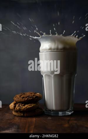 Milch in einem Glas spritzen und Schokoladenkekse auf einem Holztisch Stockfoto