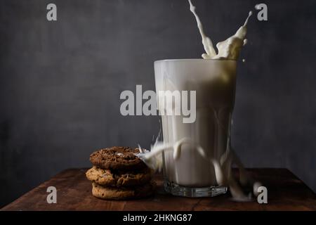 Milch in einem Glas spritzen und Schokoladenkekse auf einem Holztisch Stockfoto