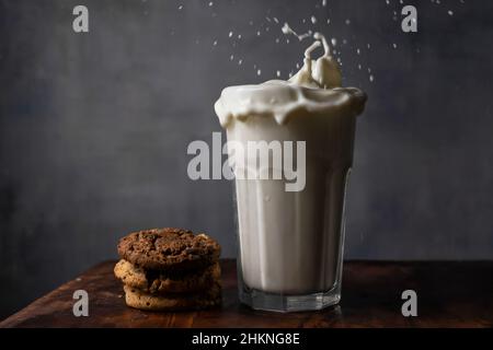 Milch in einem Glas spritzen und Schokoladenkekse auf einem Holztisch Stockfoto