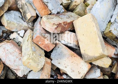 Ein Haufen alter gebrauchter Ziegelsteine mit Kratzern und Rissen von der alten Mauer in der Nähe des Grundstücks. Stockfoto