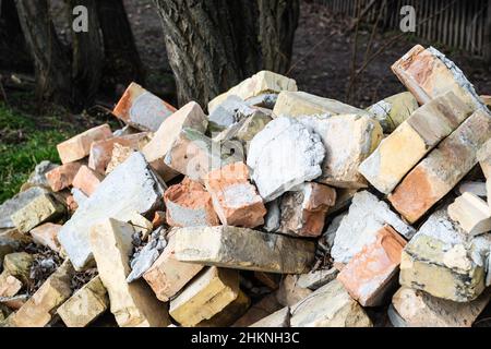 Ein Haufen alter gebrauchter Ziegelsteine mit Kratzern und Rissen von der alten Mauer in der Nähe des Grundstücks. Stockfoto