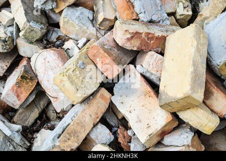 Ein Haufen alter gebrauchter Ziegelsteine mit Kratzern und Rissen von der alten Mauer in der Nähe des Grundstücks. Stockfoto